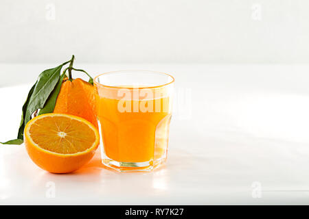An inviting glass full of orange juice, a orange divided in two and a whole one with leaf on a white background Stock Photo