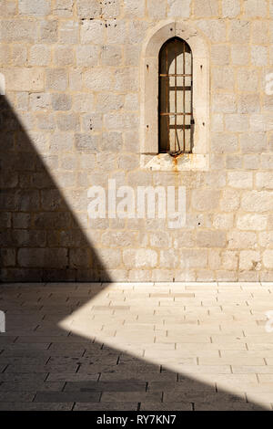 A small arched window with rusty bars across it and a shadow cast by the sun in an old town side street, Dubrovnik, Croatia Stock Photo