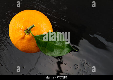 Orange with leaf shot from above on a black  wet slate plate with reflected light effects Stock Photo