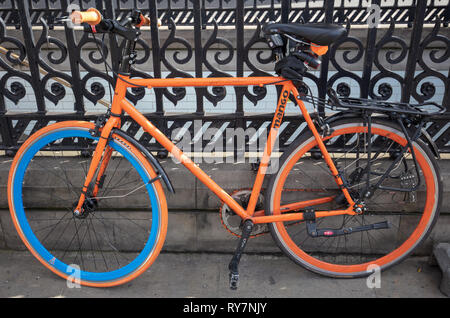 Orange bicycle chained against a cast iron railing alongside the road in London, UK. Stock Photo