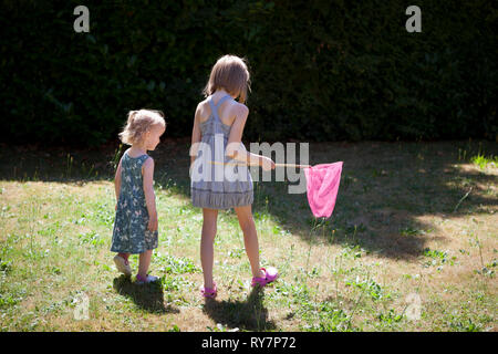Two children in a back yard hunting for butterflies with a butterfly net Stock Photo