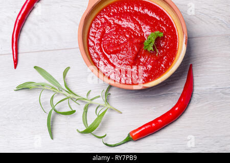 Homemade tomato sauce in bowl with rosemary and chili peppers, top-down food styling Stock Photo