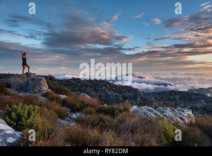A young woman practices yoga on Table Mountain at sunset, Cape Town, Western Cape, South Africa