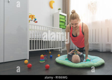 young woman doing push ups at home while playing with her little baby