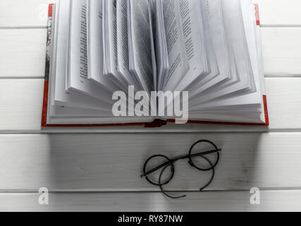 Open book ready to read lies on a white wood table next to the old round glasses. closeup Stock Photo