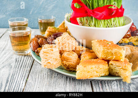 Happy Nowruz holiday background. Celebrating Nowruz sweets and treats- baklava, various dried fruits,  nuts, seeds, wooden background with green grass Stock Photo