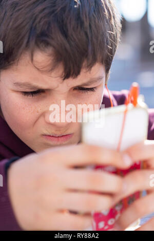Close-up of boy using smart phone while sitting outdoors during sunny day Stock Photo