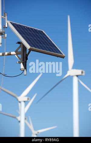 Low angle view of solar panel against windmills and clear sky during sunny day Stock Photo