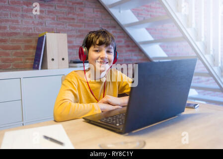 Portrait of smiling boy using headphones and laptop computer while studying at home Stock Photo