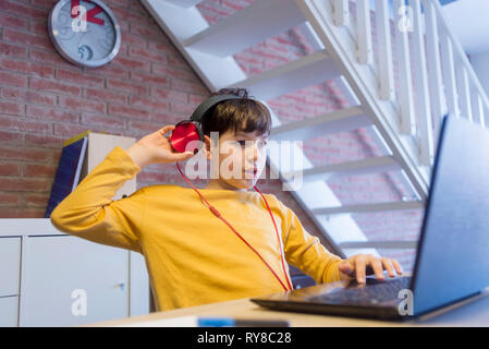 Boy doing homework using headphones and laptop computer at home Stock Photo