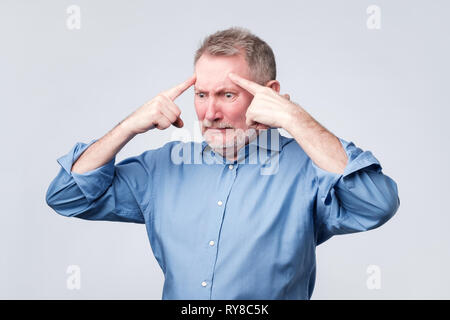 Mature european man holds fingers on temples, trying to remember something. Stock Photo