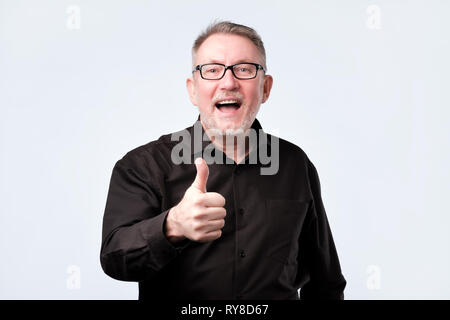 senior handsome man in black shirt and glasses showing thumbs up gesture Stock Photo