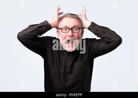 senior man eyes mouth wide open, hands in air yelling screaming shouting Stock Photo