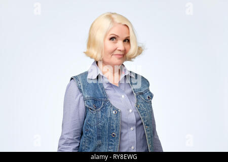 Senior woman in jeans vest and blue shirt is smiling with disbelief in her eyes. Stock Photo