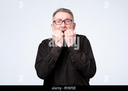 Nervous senior man in glasses bites nails, looks worried before visiting doctor Stock Photo