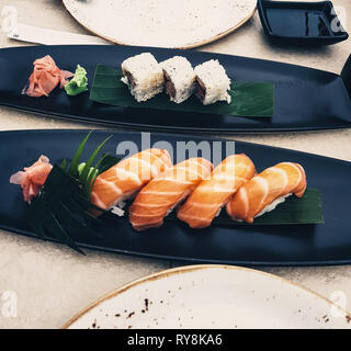 Plates of salmon sushi, nigiri and uramaki in a restaurant. Japanese cuisine with soy sauce and wasabi - raw seafood Stock Photo
