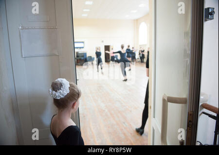 little russian ballerina looking through open doorway on dancing rehearsal of senior girls dance class Stock Photo