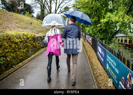 People heading for the races at Cheltenham use brolleys as they arrive at Cheltenham racecourse on the Gloucestershire Warwickshire Steam Railway from Toddington, where a special heritage steam express train service is taking race goers to Cheltenham. Stock Photo