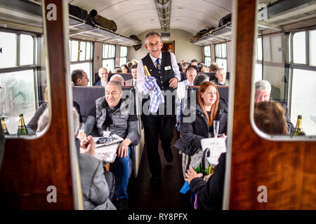 People heading for the races at Cheltenham are served champagne in a period carriage on the Gloucestershire Warwickshire Steam Railway from Toddington, where a special heritage steam express train service is taking race goers to Cheltenham. Stock Photo