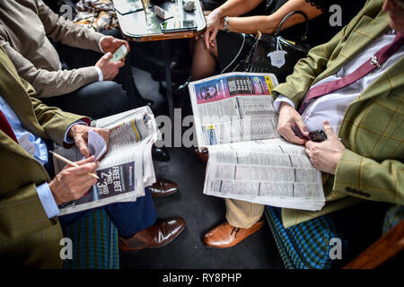People heading for the races at Cheltenham check the form as they ride in a period carriage on the Gloucestershire Warwickshire Steam Railway from Toddington, where a special heritage steam express train service is taking race goers to Cheltenham. Stock Photo