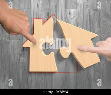 Man and woman two hands assembling wooden house shape puzzles, high angle view, on wood plank background. Stock Photo
