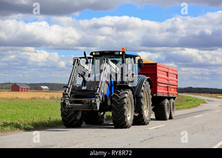 Ilmajoki, Finland - August 11, 2018: Blue Valtra farm tractor pulls trailer load of harvested grain along rural road on a clear day of autumn harvest. Stock Photo