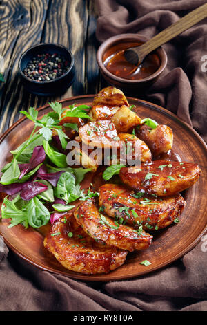 grilled sticky glazed Pork cutlets with baked Potatoes served with fresh green salad on earthenware plate on an old wooden rustic table with brown clo Stock Photo