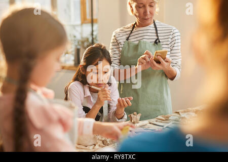 Portrait of Asian girl enjoying pottery class with group of children in workshop, copy space Stock Photo