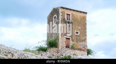 The white ruined rocks of the theatre in Neapolis in Siracusa Sicily Italy and the tall tower house on the top Stock Photo