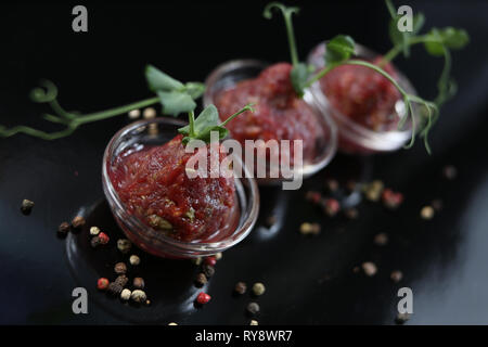 Red appetizing Tartar sauce in three pialas, decorated with a stem of sprouted green peas, close-up, for a menu Stock Photo