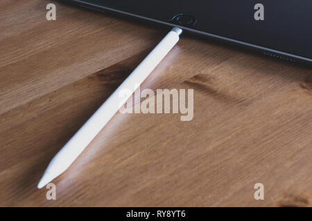 Apple Pencil 2015 1st generation connected to iPad Pro charging on natural wooden table Stock Photo