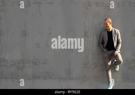 Cool guy leaning against a grey painted wooden wall, drizzled in sunlight Stock Photo