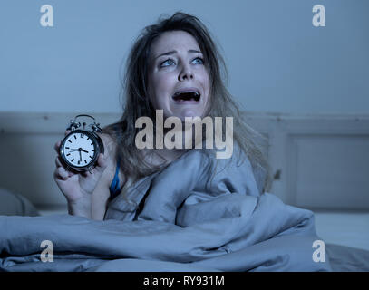 Sleepless and desperate beautiful caucasian woman awake at night not able to sleep, showing clock, feeling frustrated and worried suffering from insom Stock Photo