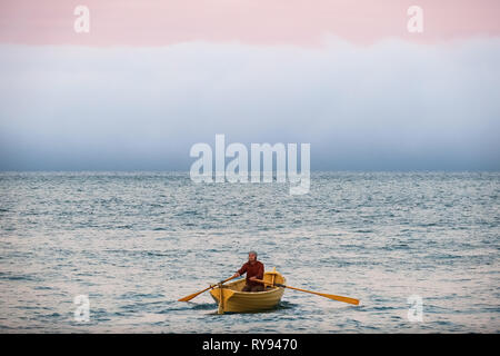 Boat Man in Yellow Row boat, With Pink Sunset and Fog - Sausalito, California Stock Photo