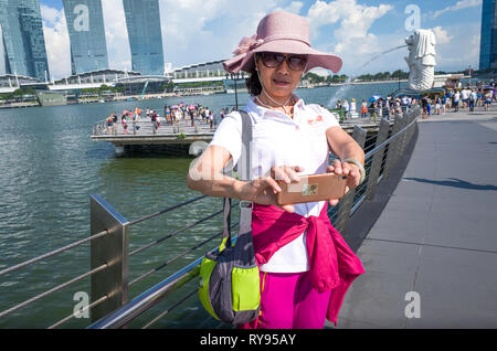 Korean tourist woman in Pink Sunhat, taking selfie with Merlion statue and Marina Bay Sands, Singapore Stock Photo