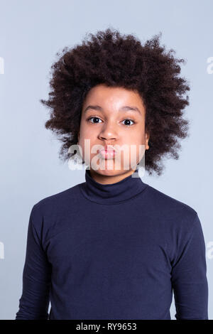 African American dark-haired kid inflating cheeks while wearing blue turtleneck Stock Photo
