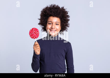 Smiling positive dark-haired child carrying colorful candy on wooden stick Stock Photo