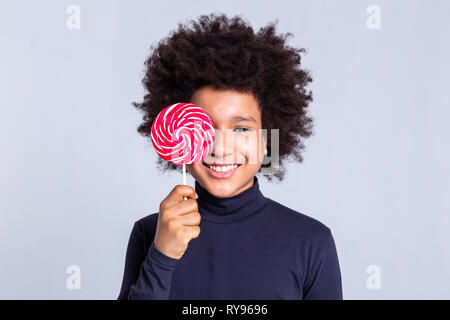 Cheerful African American kid with wild hair covering face with big candy Stock Photo