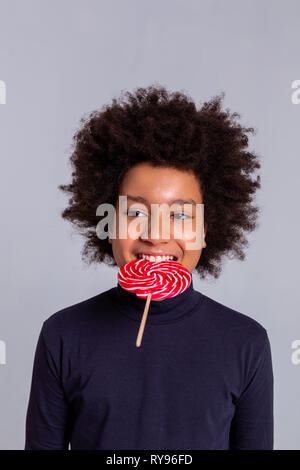 Funky dark-haired curly boy biting hard candy with strong teeth Stock Photo