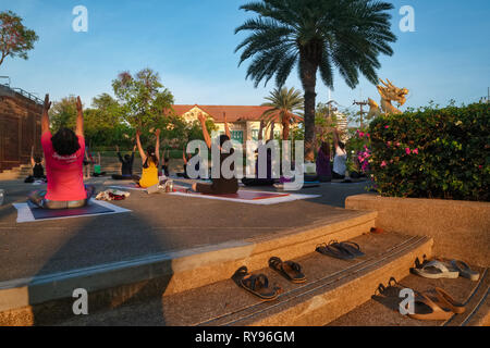 An evening yoga and meditation class in progress at 72nd Anniversary Queen Sirikit Park with its dragon monument (r), in Phuket Town, Thailand Stock Photo