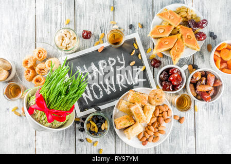 Happy Nowruz holiday background. Celebrating Nowruz sweets and treats- baklava, various dried fruits,  nuts, seeds, wooden background with green grass Stock Photo