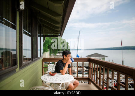 Man drinking coffee looking at lake while sitting in balcony against sky Stock Photo