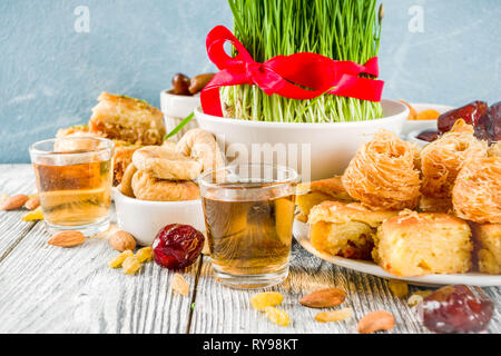 Happy Nowruz holiday background. Celebrating Nowruz sweets and treats- baklava, various dried fruits,  nuts, seeds, wooden background with green grass Stock Photo