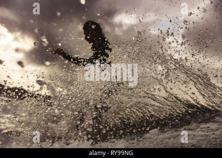 Black and white side view of female floating on surf board between water of sea with splashes on Bali, Indonesia Stock Photo