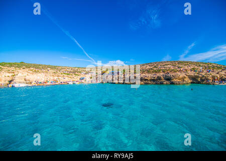 Comino, Malta - November, 2018: Tourists crowd at Blue Lagoon to enjoy the clear turquoise water on a sunny summer day with clear blue sky and boats Stock Photo