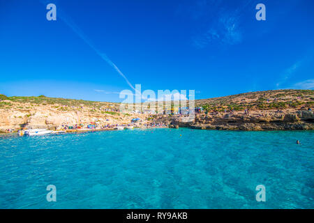 Comino, Malta - November, 2018: Tourists crowd at Blue Lagoon to enjoy the clear turquoise water on a sunny summer day with clear blue sky and boats Stock Photo