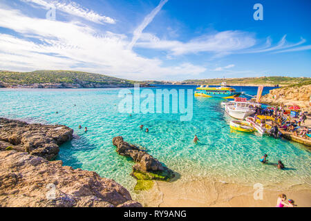 Comino, Malta - November, 2018: Tourists crowd at Blue Lagoon to enjoy the clear turquoise water on a sunny summer day with clear blue sky and boats Stock Photo