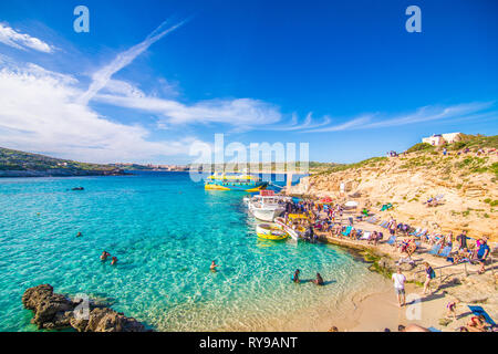 Comino, Malta - November, 2018: Tourists crowd at Blue Lagoon to enjoy the clear turquoise water on a sunny summer day with clear blue sky and boats Stock Photo