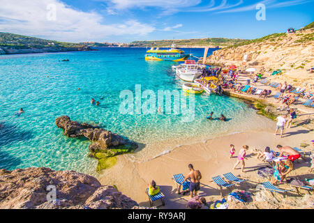 Comino, Malta - November, 2018: Tourists crowd at Blue Lagoon to enjoy the clear turquoise water on a sunny summer day with clear blue sky and boats Stock Photo