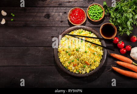 Cooked white rice with curry and vegetables in a pan with chopsticks on a black wood background. Stock Photo